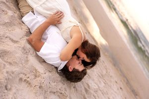 Couple sharing a kiss while lying together on sandy beach.