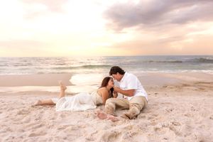 Couple sitting closely together on sandy beach at golden sunset, sharing an intimate romantic moment.