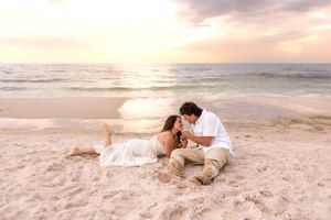 Couple sitting together on beach sand at golden sunset by ocean.