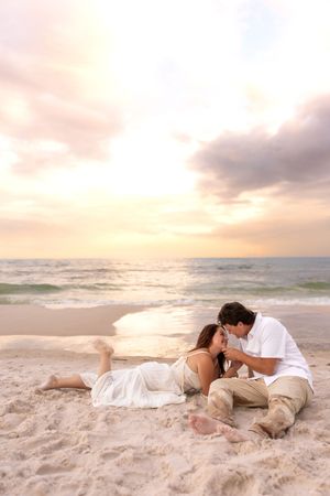 Romantic couple kissing while lying on sandy beach at golden sunset.
