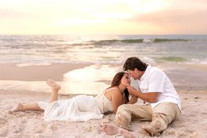 Romantic couple sharing a tender moment lying on a sandy beach at a pastel sunset.