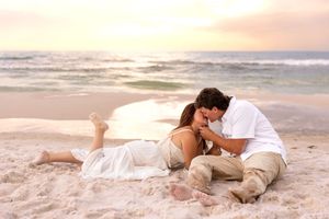 Romantic couple sharing a tender moment on a sandy beach at sunset, with gentle ocean waves in the background.