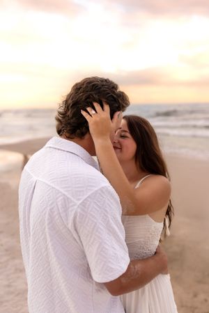 Couple sharing a tender kiss on the beach at sunset, woman's hand in man's curly hair.