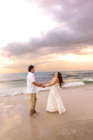 Couple holding hands and dancing together on beach at colorful sunset.