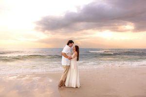 Romantic couple embracing on beach at sunset with dramatic cloudy sky and ocean waves.