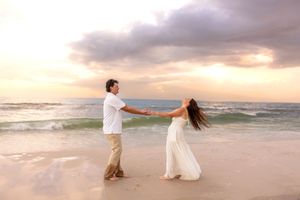 Couple holding hands facing each other on a serene beach at golden sunset with gentle ocean waves.