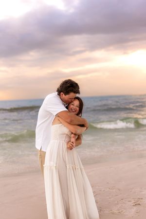 Happy couple embracing and laughing on beach at golden sunset.