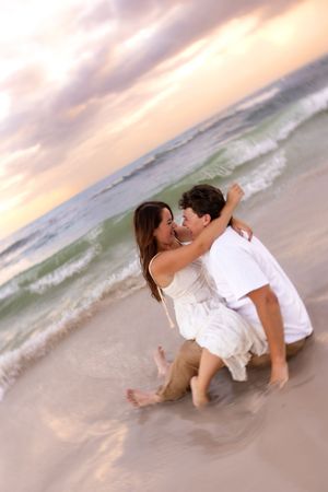 Romantic couple embracing and almost kissing on a beach at sunset, sitting in the shallow ocean waves.