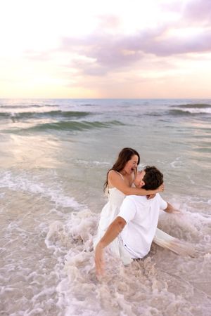 Romantic couple embracing in ocean waves at sunset on sandy beach.