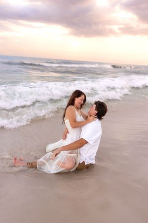 Romantic couple laughing and embracing in ocean waves at sunset on a sandy beach.