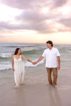 Romantic couple holding hands while standing in ocean waves at colorful sunset beach.