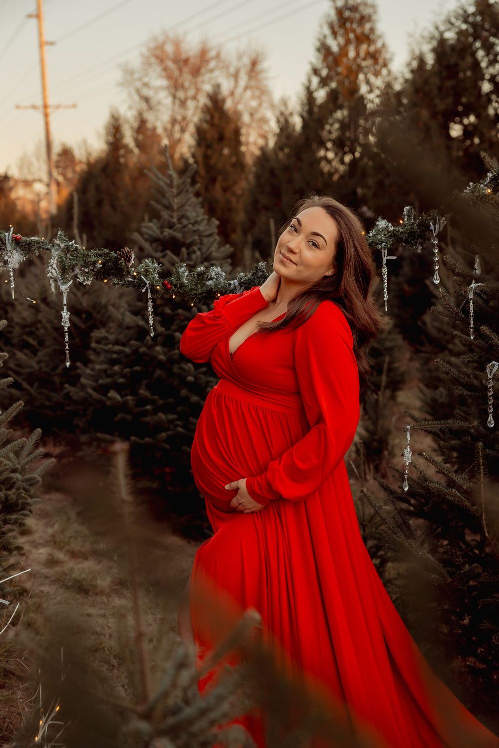Pregnant woman in red dress at Christmas tree farm.