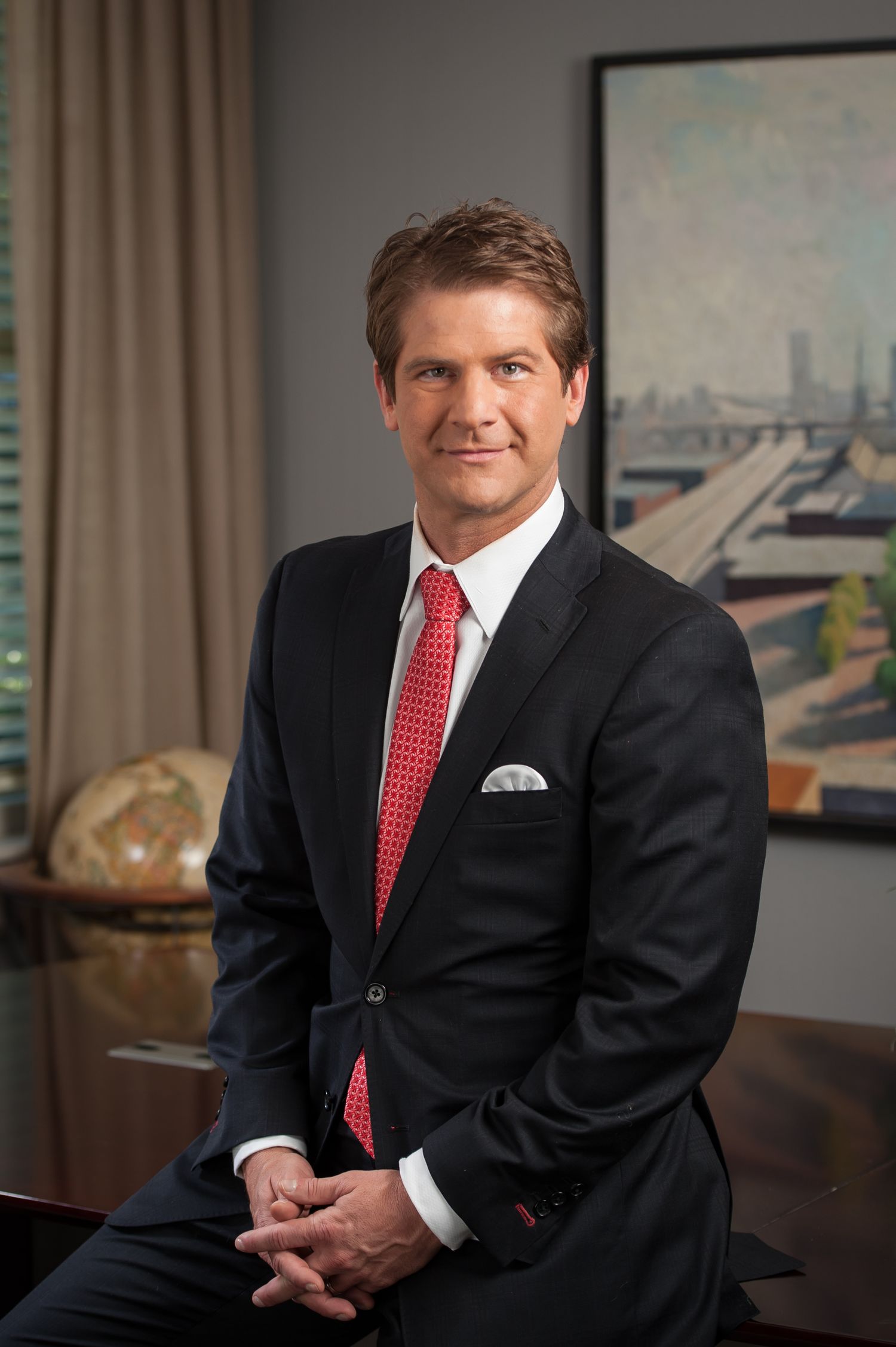 Professional man in blue plaid suit with arms crossed smiling confidently outdoors near columns.