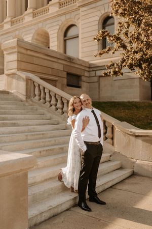 Bride and groom pose on grand stone staircase of elegant building in warm golden hour light.