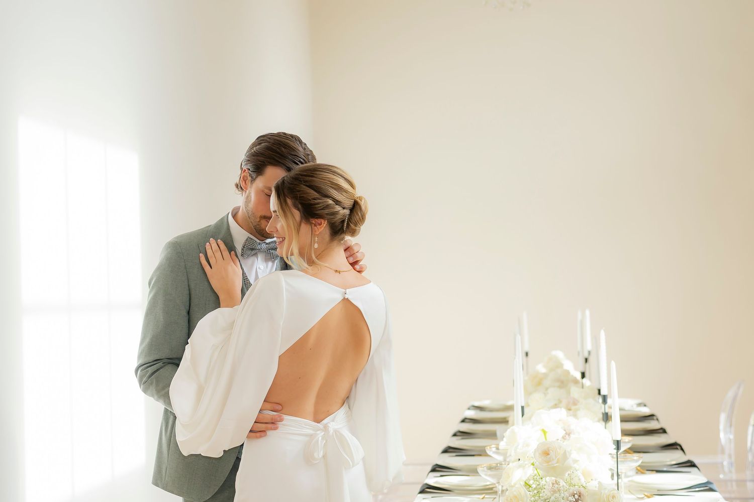 Elegant bride and groom sharing an intimate embrace near a beautifully set reception table with candles.