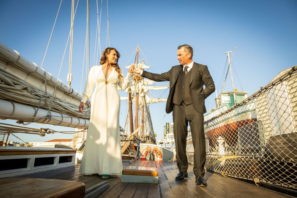 Bride and groom toasting on a historic tall ship deck at sunset during a nautical wedding celebration.