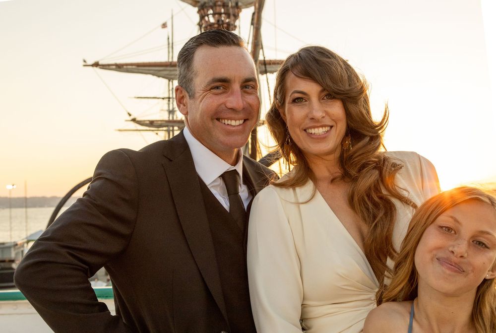 Smiling couple in wedding attire posing at sunset on a boat with a guest.