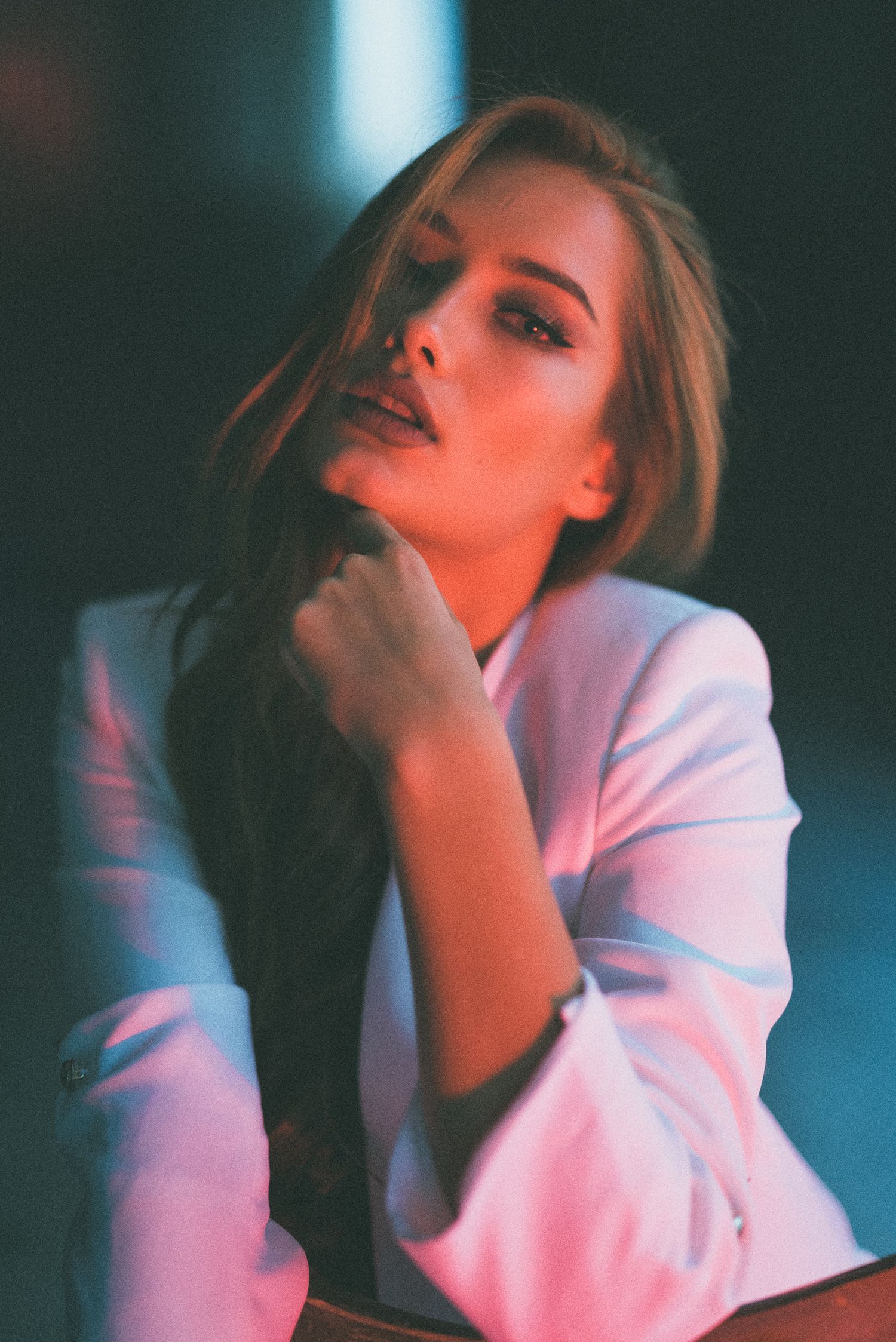 Ritratto d'atmosfera di una donna con lunghi capelli scuri e blazer chiaro, illuminata da suggestivi riflessi di luce calda e azzurra al neo