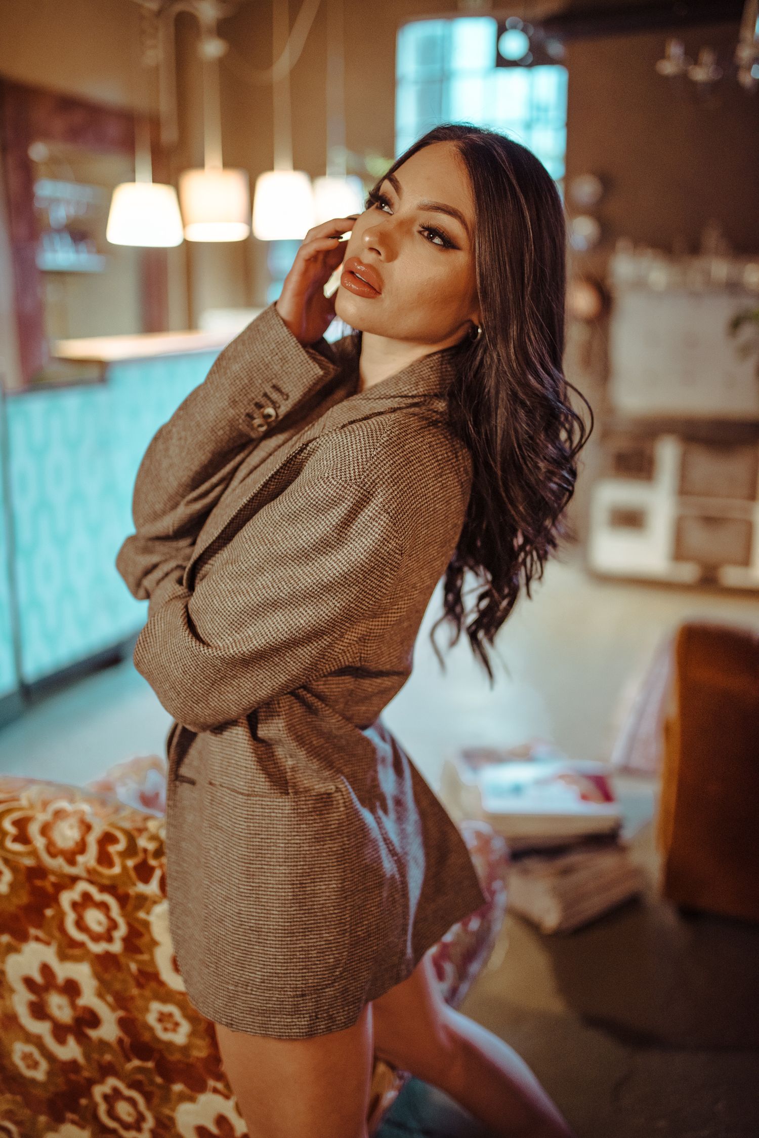 Posa sofisticata di una donna con blazer marrone oversized e capelli mossi, fotografata all'interno di un locale dal design retrò.