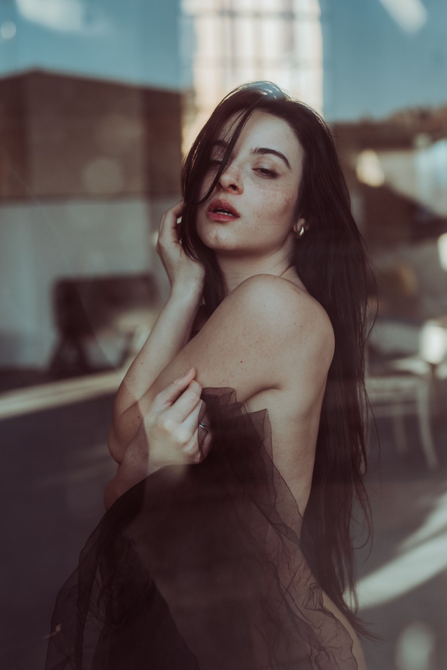 Scatto artistico di una donna con lunghi capelli scuri che avvolge un velo di tulle nero trasparente attorno al corpo, fotografata attravers
