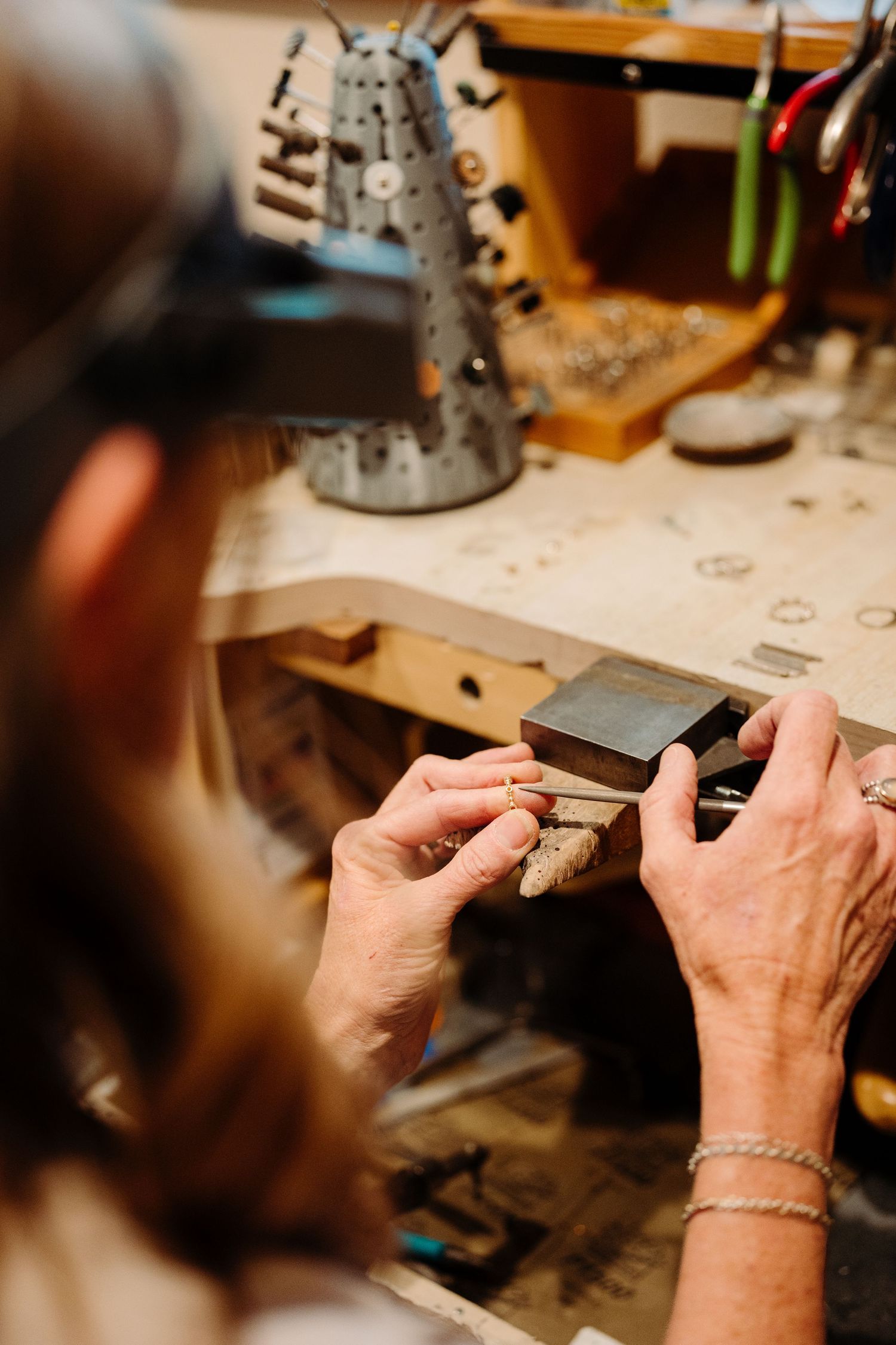 Jeweler crafting a piece at a workbench, holding small tools with a bracelet on wrist in a workshop.