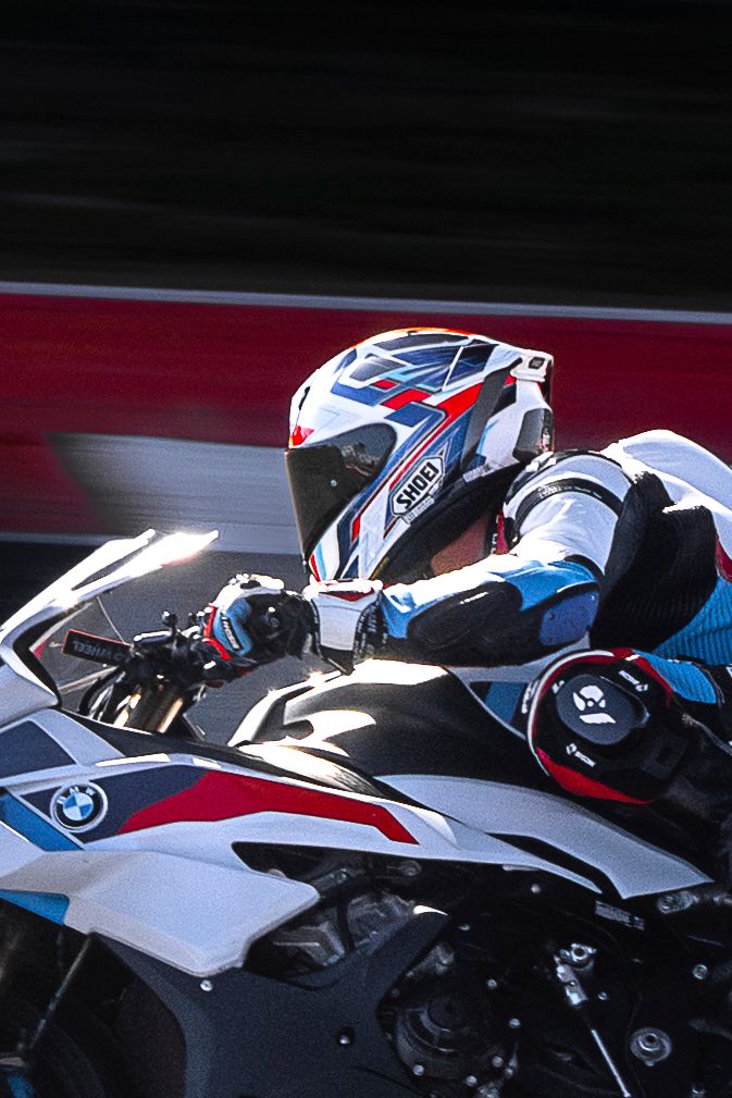A motorcyclist in full racing gear rides a BMW S1000RR sportbike at high speed on a race track.