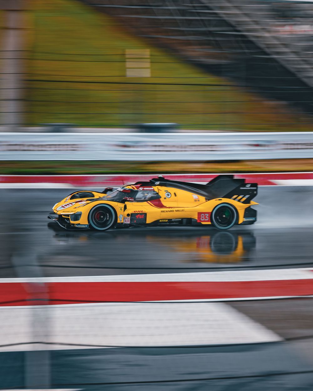 Yellow racing car speeding on wet track in rainy conditions, motion blur capturing high-speed performance on circuit.