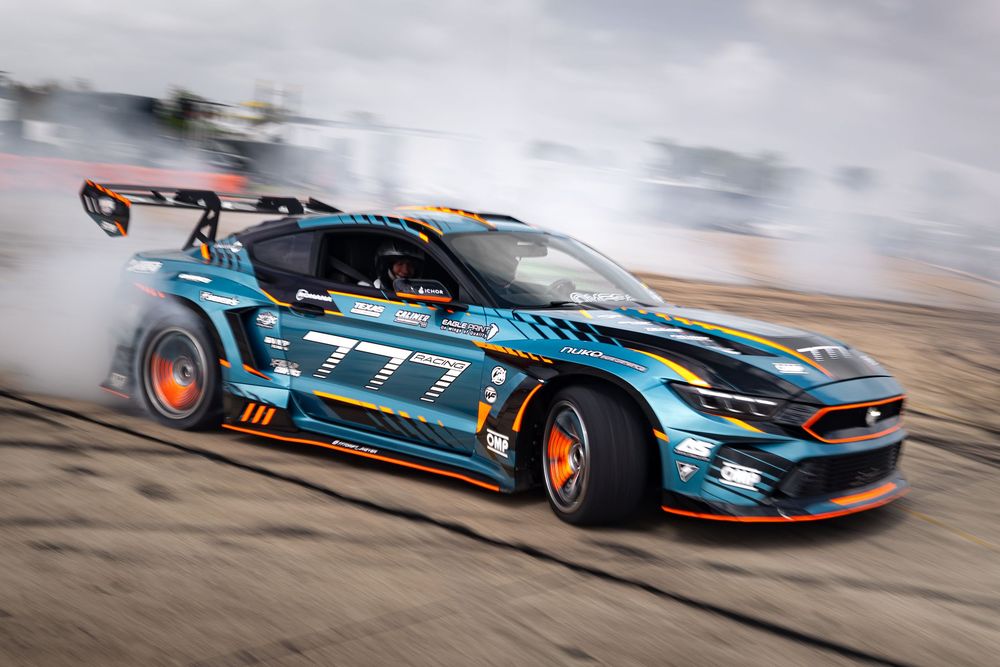 Ford Mustang #777 drift car burning tires on a race track, surrounded by smoke during a Formula Drift competition.