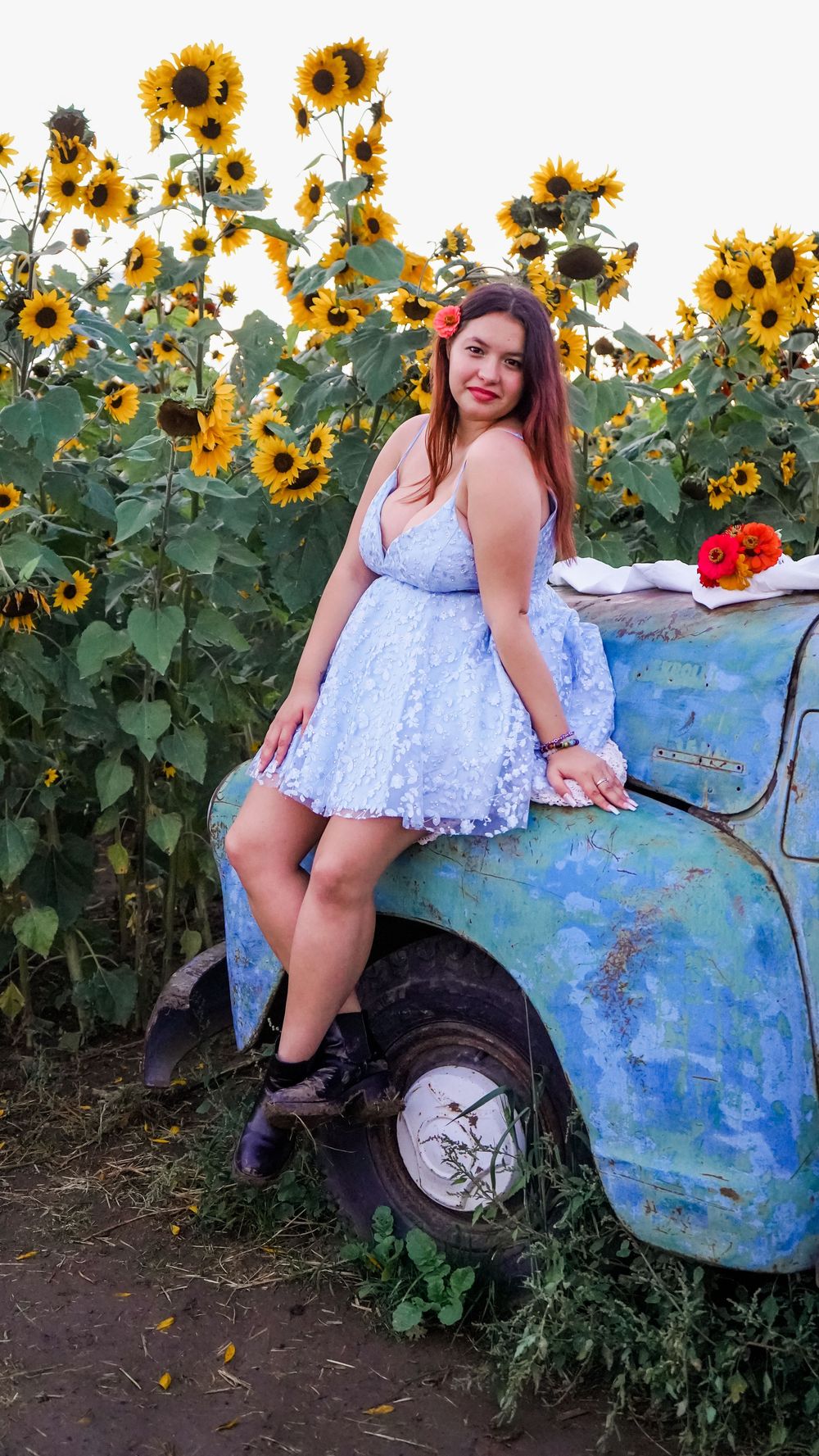 Tall sunflowers stand against a blue sky next to a rustic blue tractor in a field.