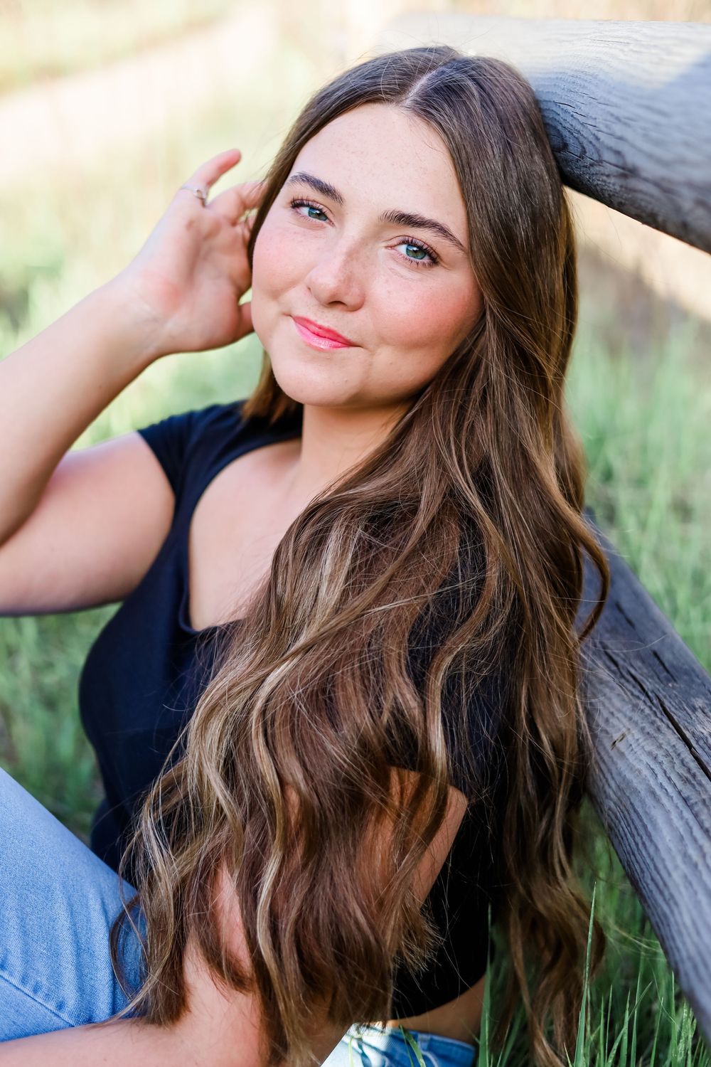 Portrait of woman with long wavy hair leaning against natural backdrop.