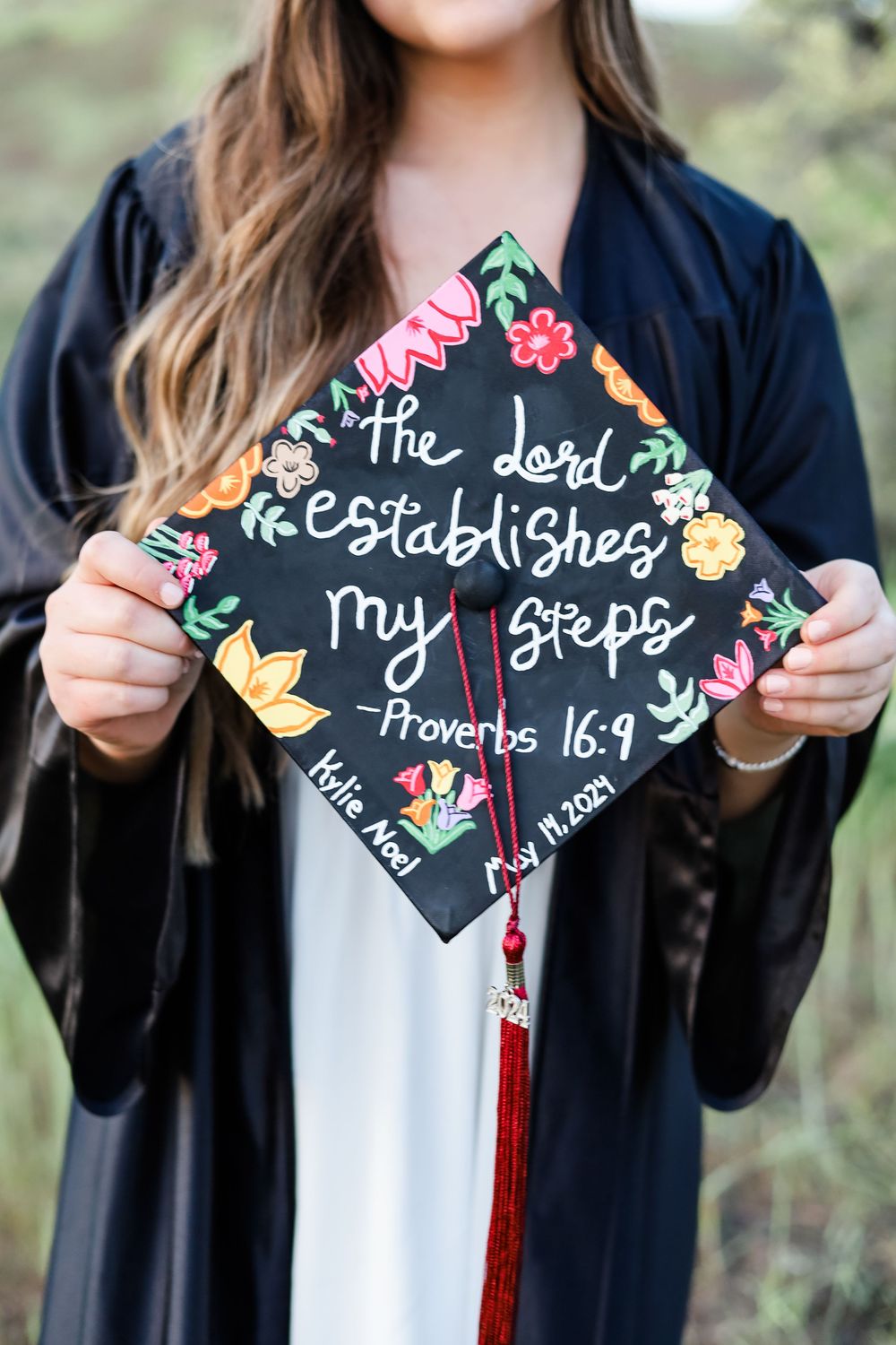 A decorated graduation cap with floral designs and a Bible verse from Proverbs.