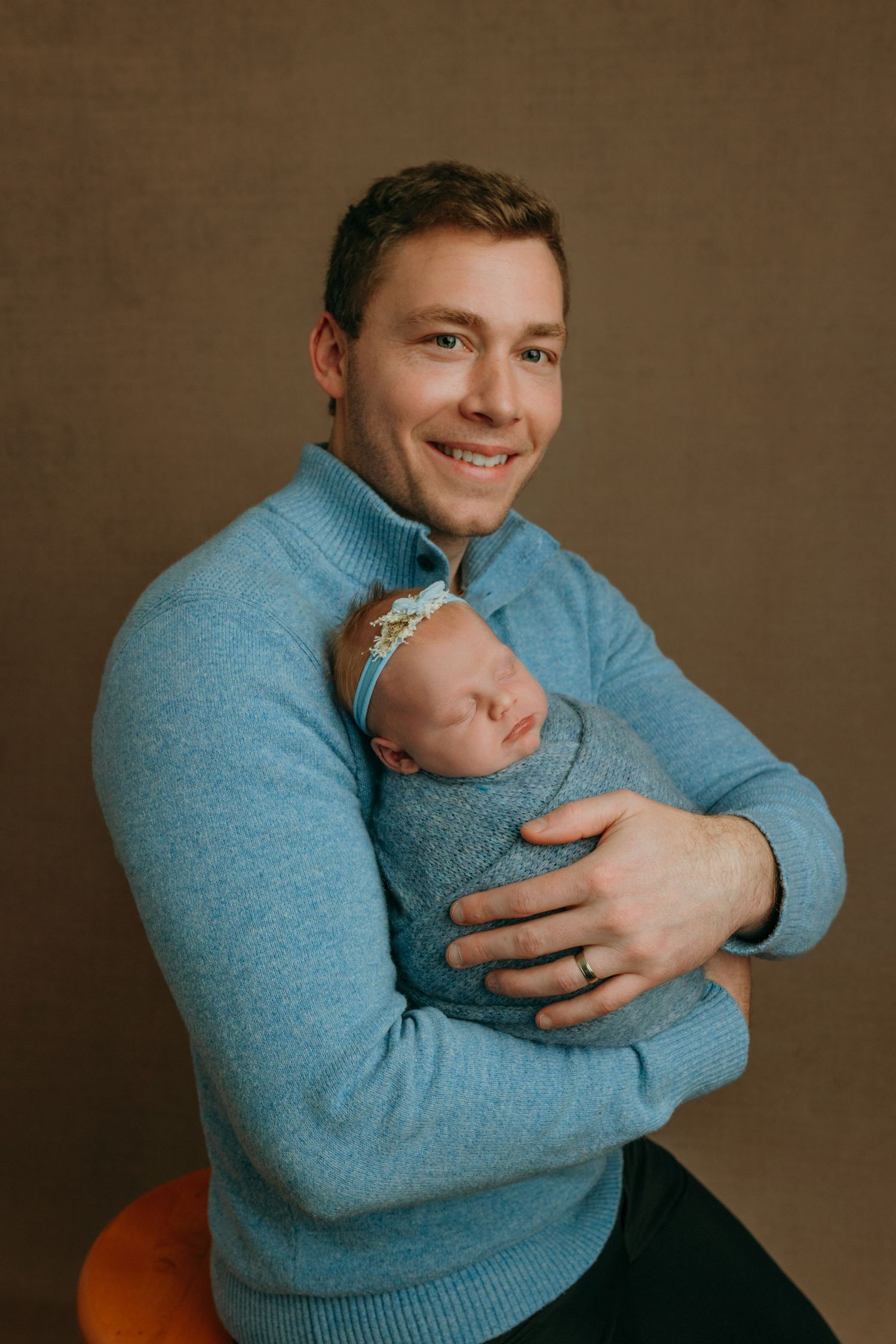 A parent in a blue sweater tenderly holds and gazes at their sleeping newborn baby in a family photography studio in Victoria BC.