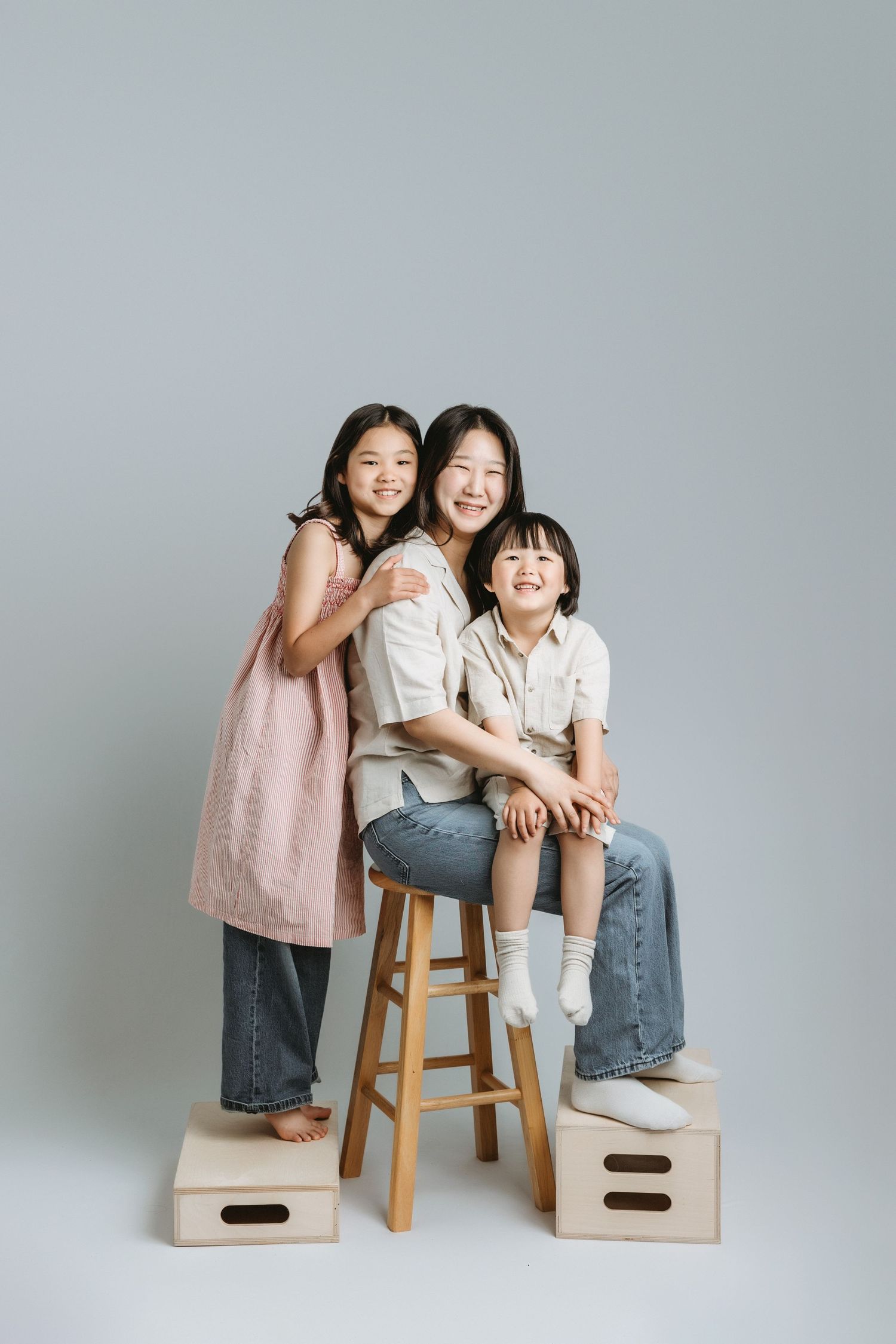 A family pose together in a studio, wearing casual outfits in shades of pink, beige, and blue jeans at the family portrait studio in YYJ.