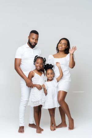 Family of four wearing all-white outfits poses together against light background in studio setting.