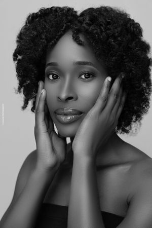 Beautiful black and white portrait of a woman with natural curly afro hair posing with hands on face.