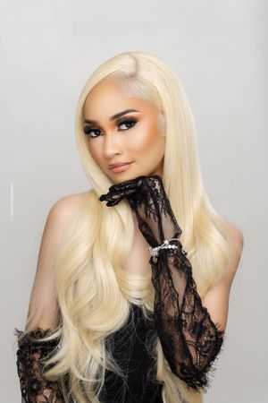 Beauty portrait with platinum blonde hair, black lace, and dramatic makeup against light background.