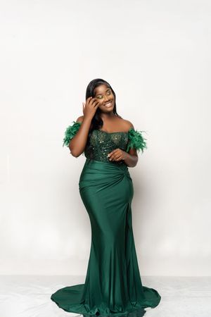 A glamorous emerald green evening gown with feather details and sequins sparkles against a white background.
