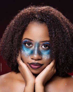 Creative beauty portrait with natural curly hair and sparkly blue eyeshadow makeup against dark background.