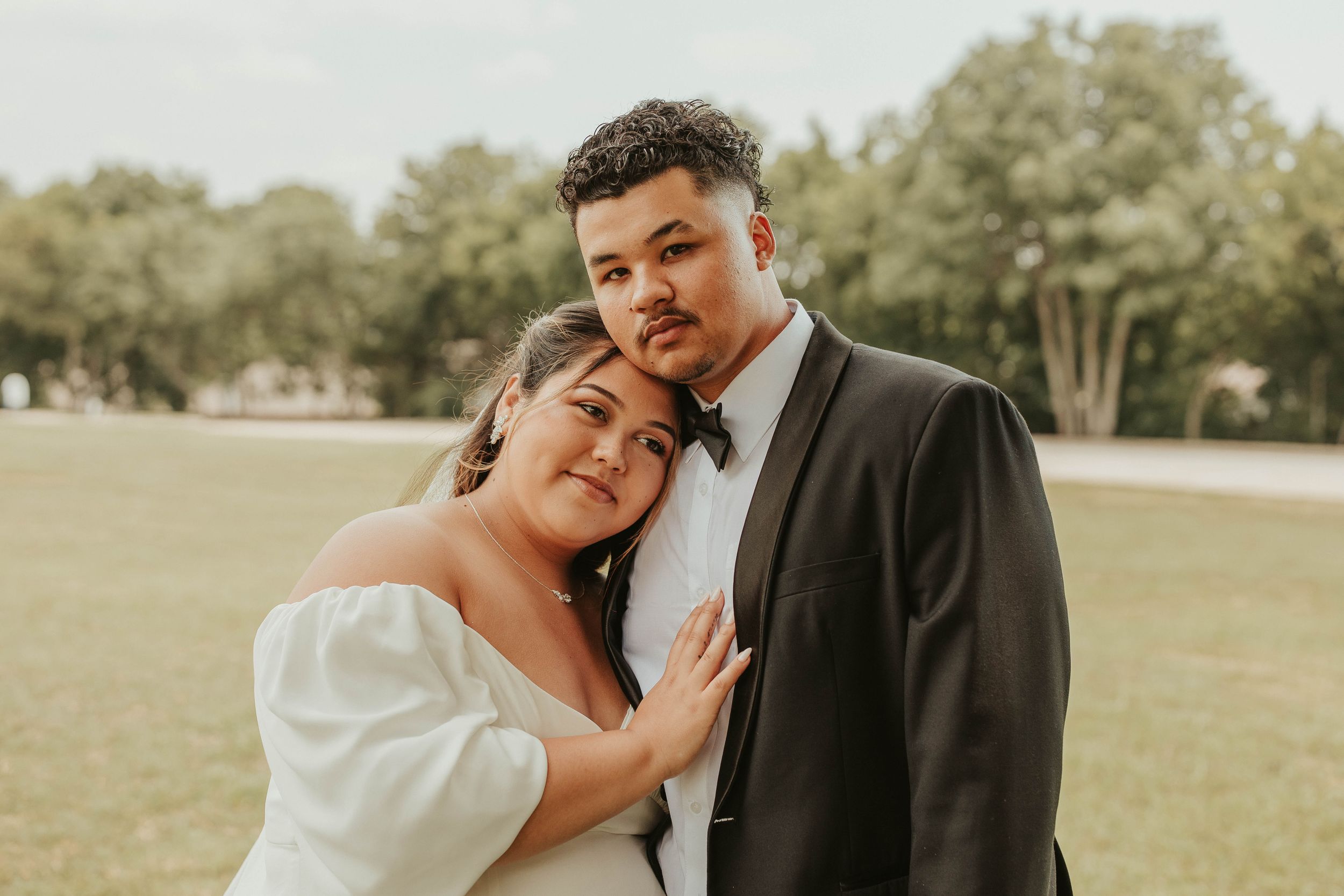 Newlywed couple in formal attire sharing an intimate moment in a sunlit park.