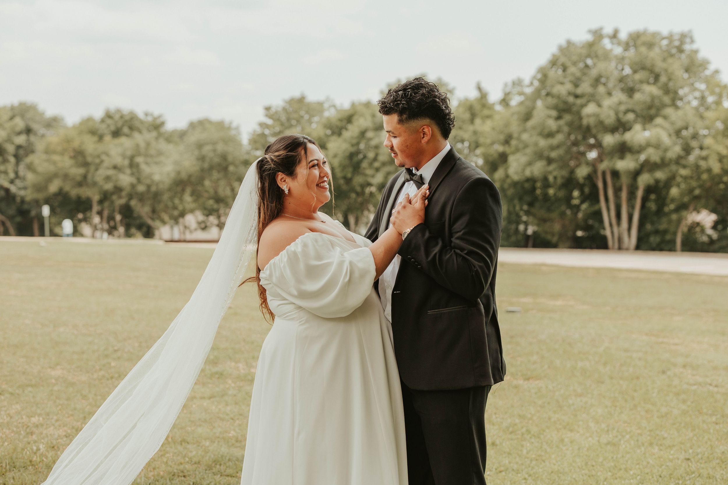 A romantic wedding portrait of newlyweds embracing in an outdoor field setting.