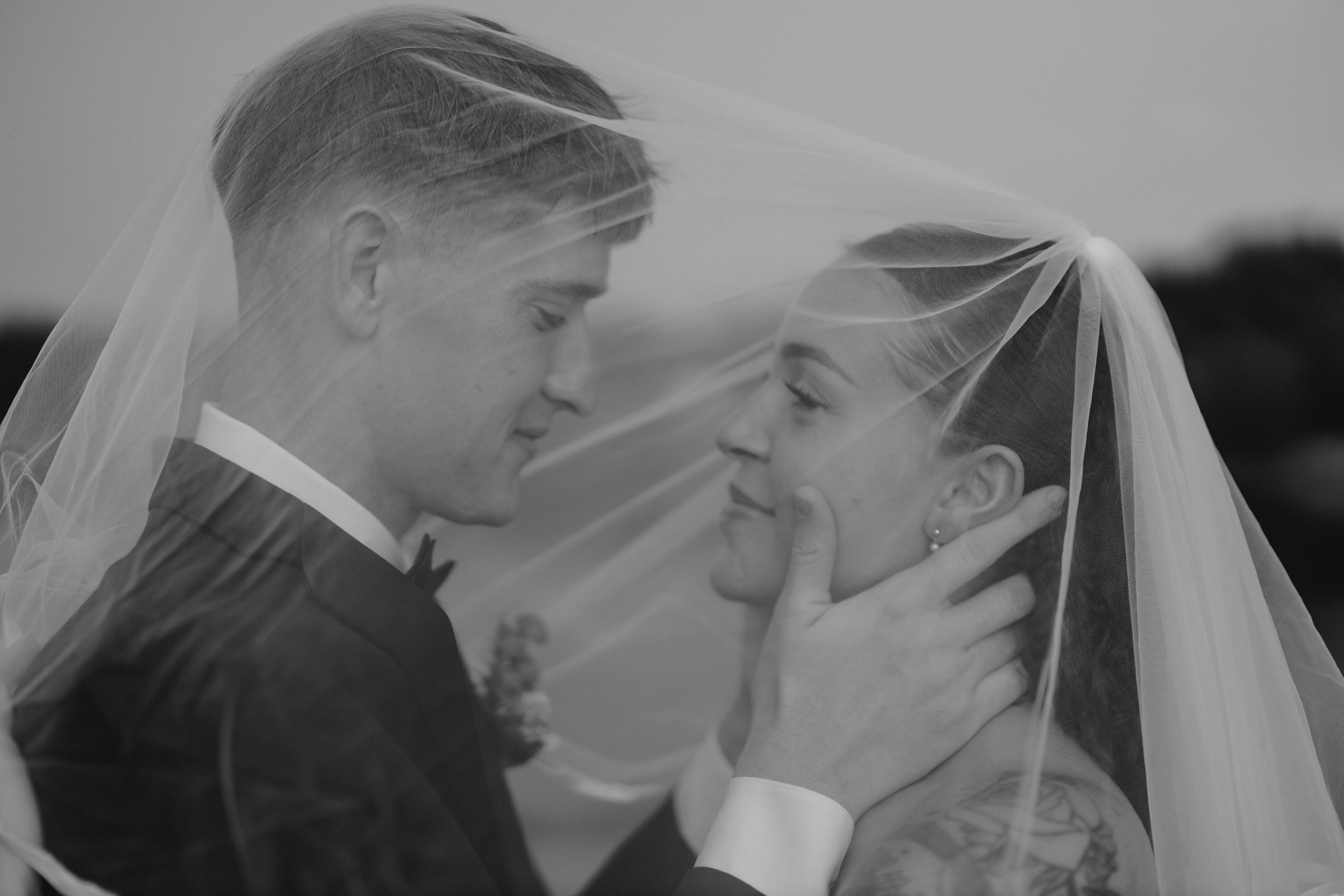 An intimate black and white wedding portrait with a flowing veil creating a soft, dreamy atmosphere.