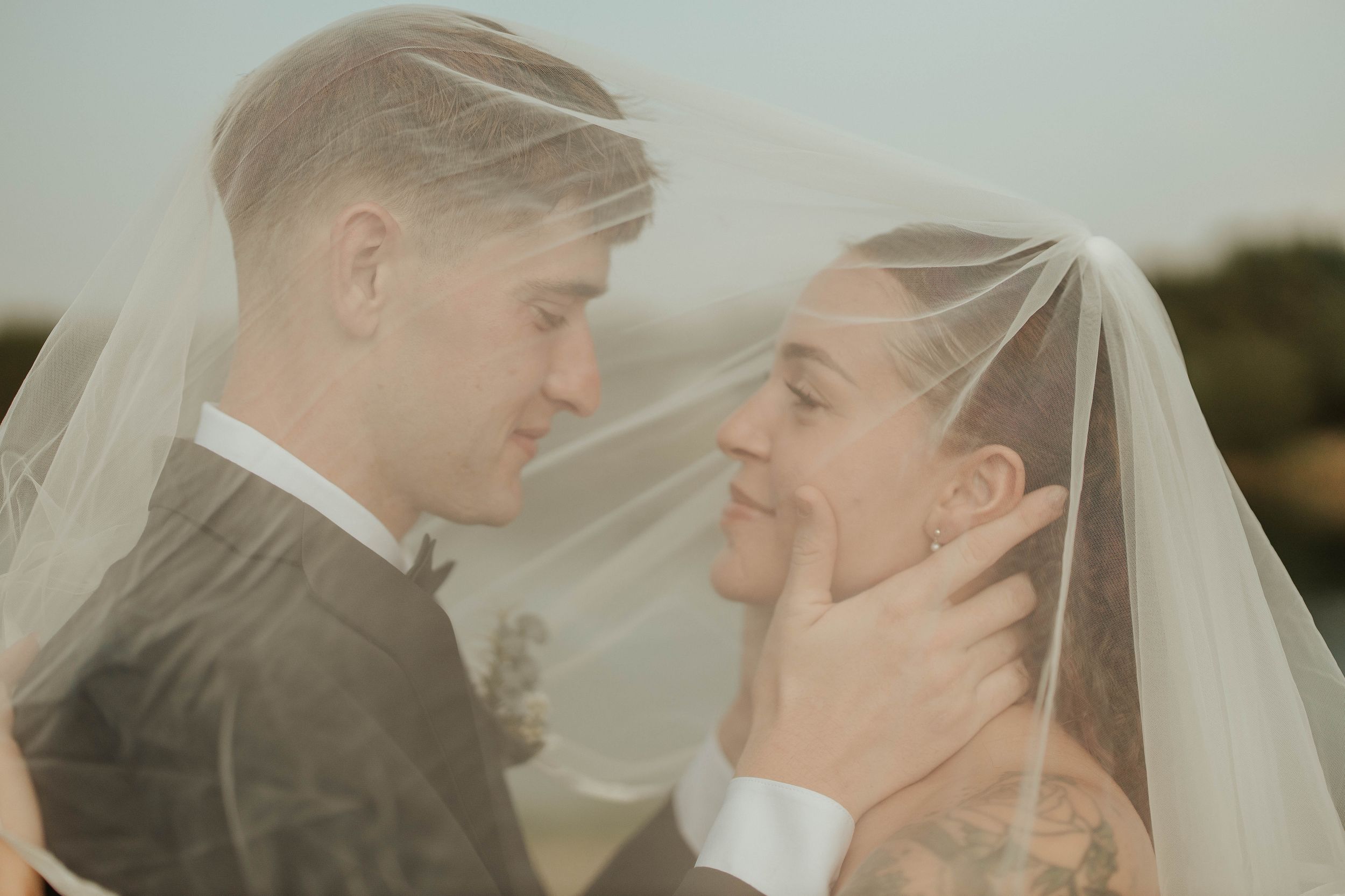 A tender wedding moment captured through a delicate veil in muted tones.