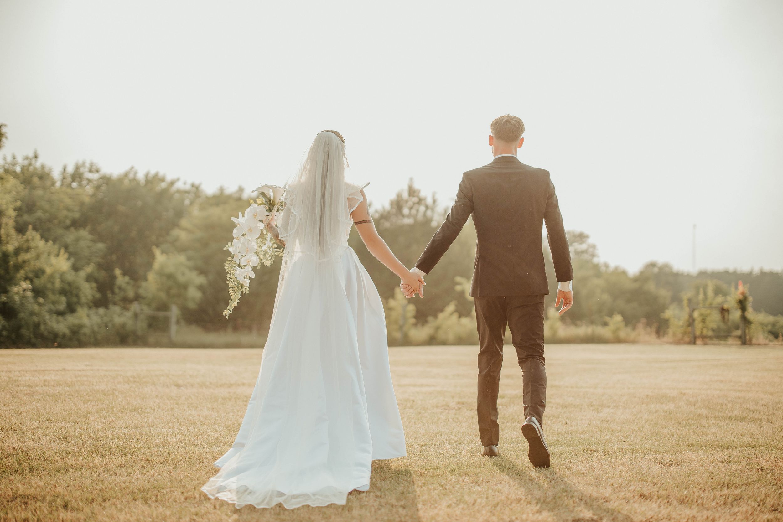 Wedding couple walking together in a sunlit field during golden hour.