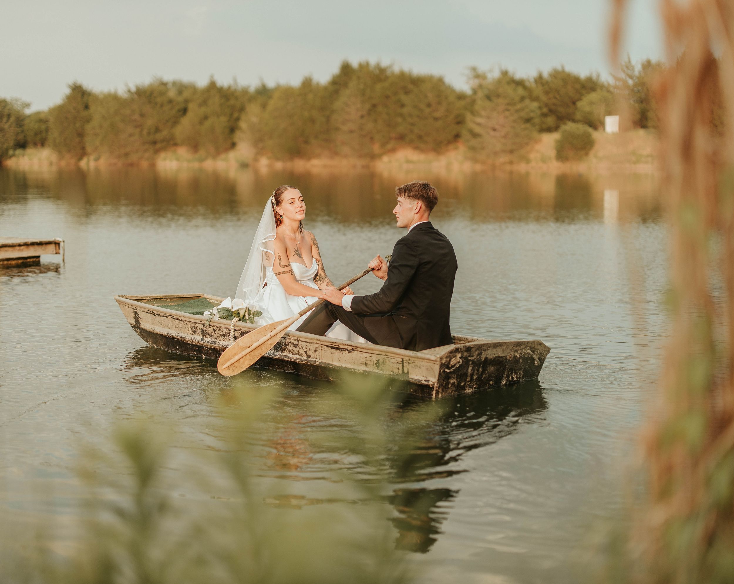 A couple seated in a wooden boat on a calm lake shares a romantic moment at sunset.