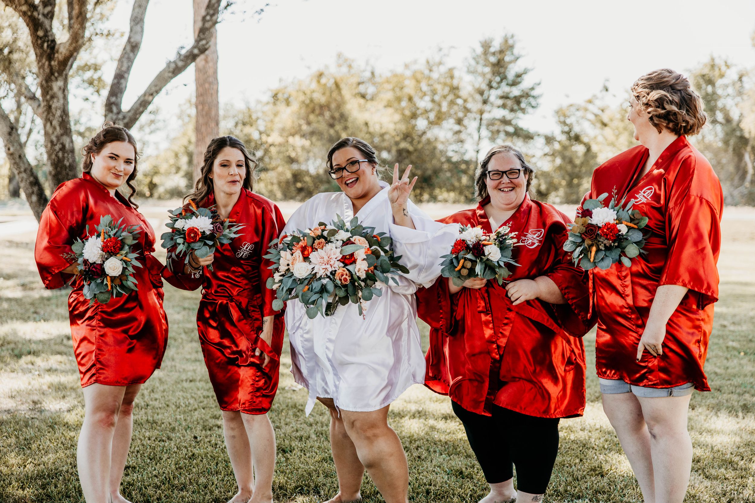 Wedding party members wearing bright red shawls pose playfully outdoors in a candid photo series.