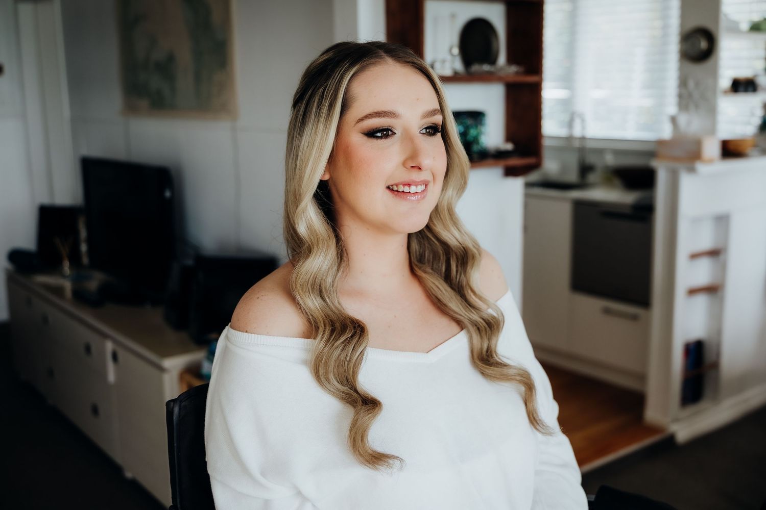 Professional stylist in white uniform carefully applies makeup with brush at bright modern beauty salon.