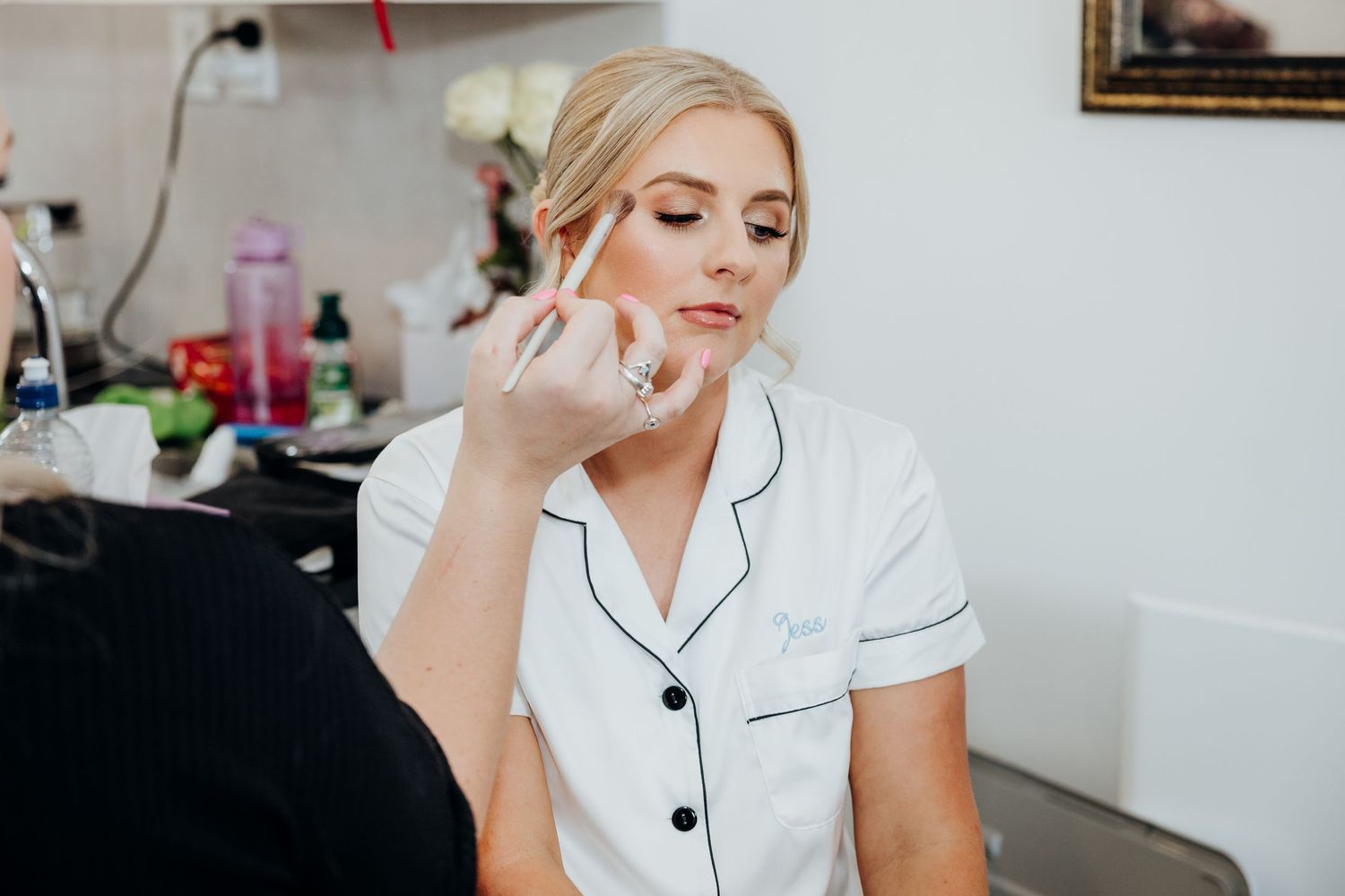 Professional stylist in white uniform carefully applies makeup with brush at bright modern beauty salon.