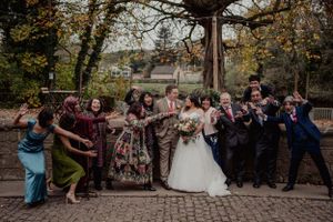 Wedding party poses for fun group photo outdoors with autumn trees in background.