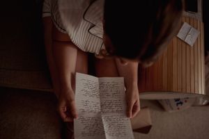 Handwritten letter held by someone sitting, captured in intimate lighting.