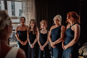 A group of bridesmaids in matching navy blue dresses stand in line during wedding preparations.